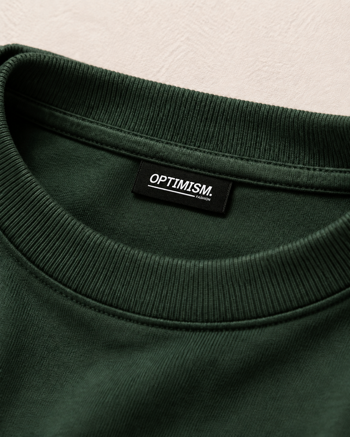 Close detail of the ribbed collar, cotton surface and interior OPTIMISM. FASHION label on the Private Green T-shirt.