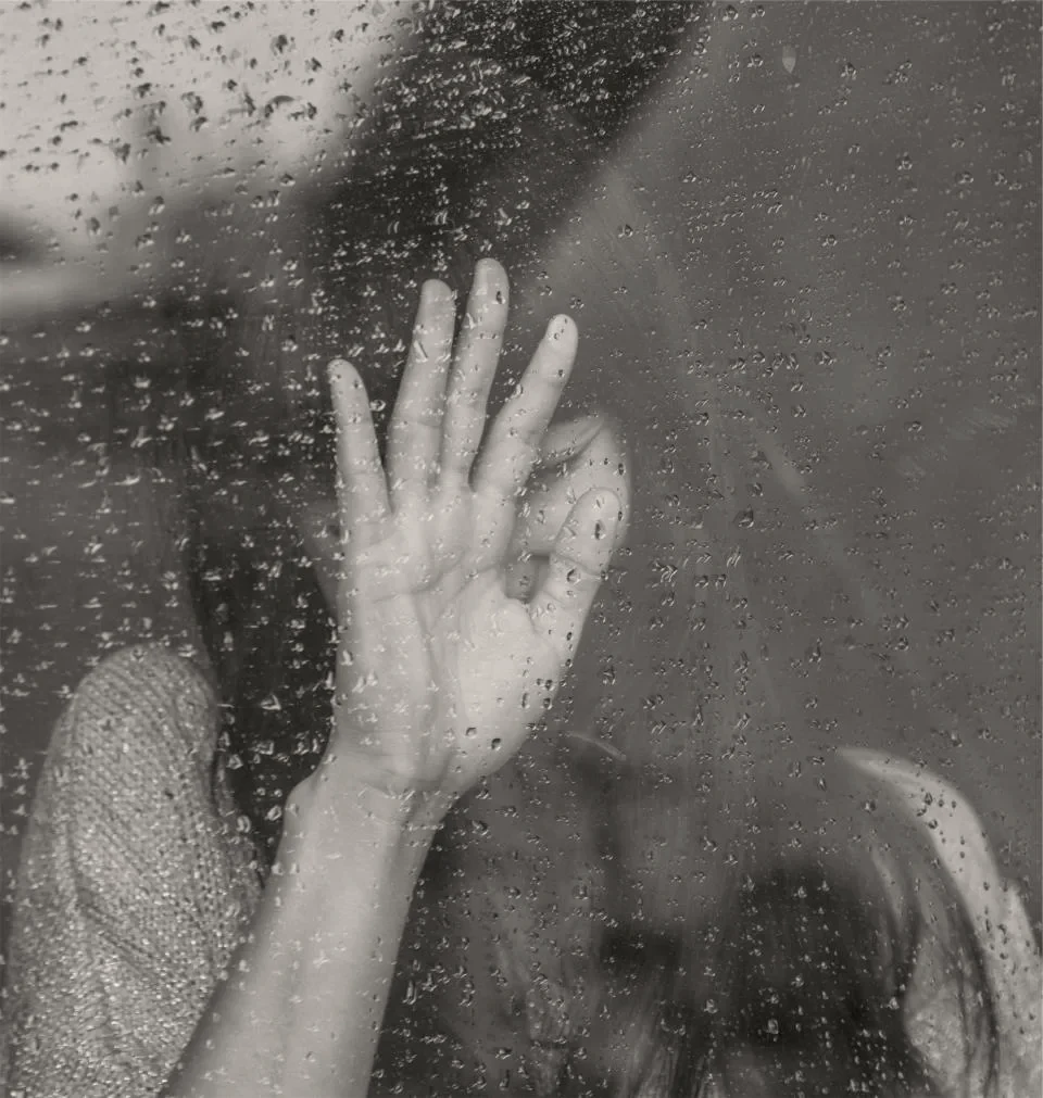 A hand pressed to a rain-covered window