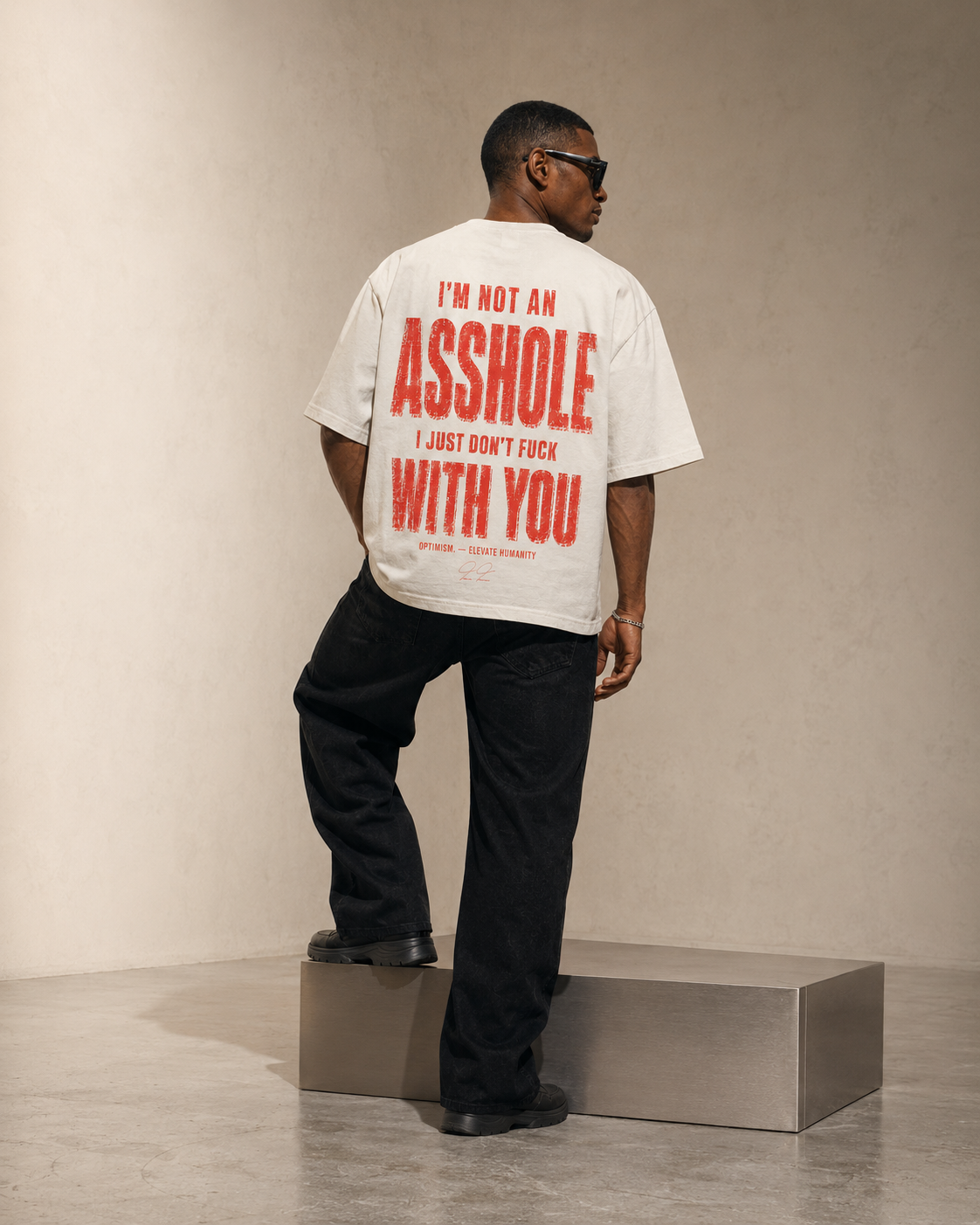 Full-length view of the bone-white OPTIMISM. Not for Everyone oversized tee worn beside a metallic bench.